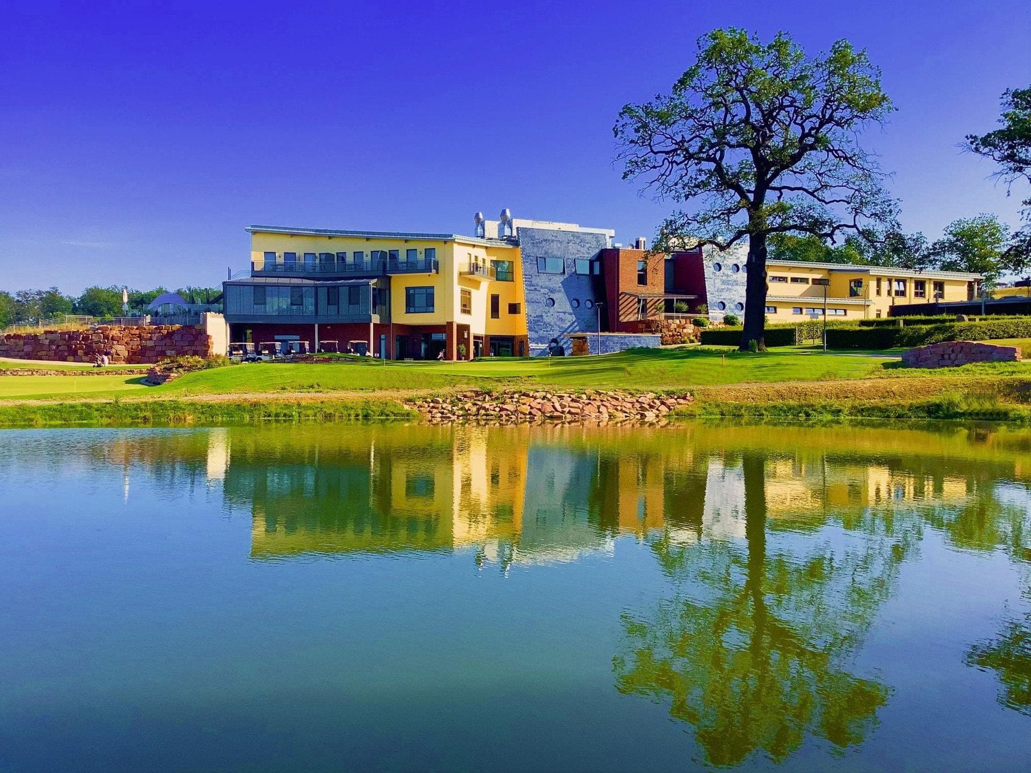 Modernes Gebäude am Wasser mit reflektierendem See und Baum im Vordergrund.